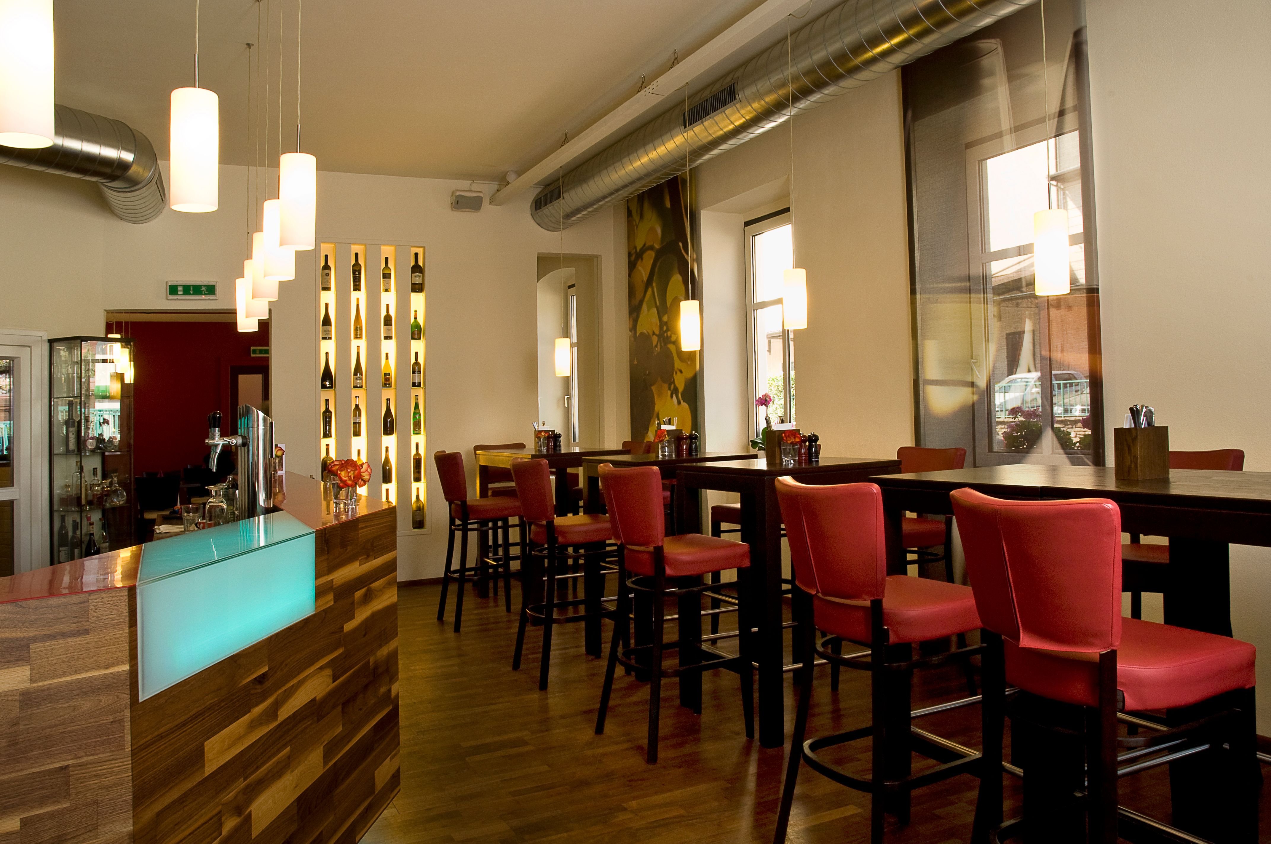Pohled do interiéru moderní restaurace s červenými židlemi a dřevěným pultem.