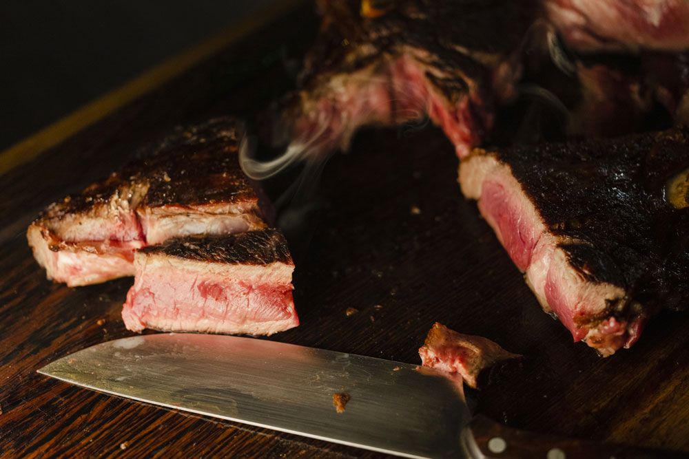 Detailní záběr na steak nakrájený na plátky na dřevěném prkénku s nožem vedle.