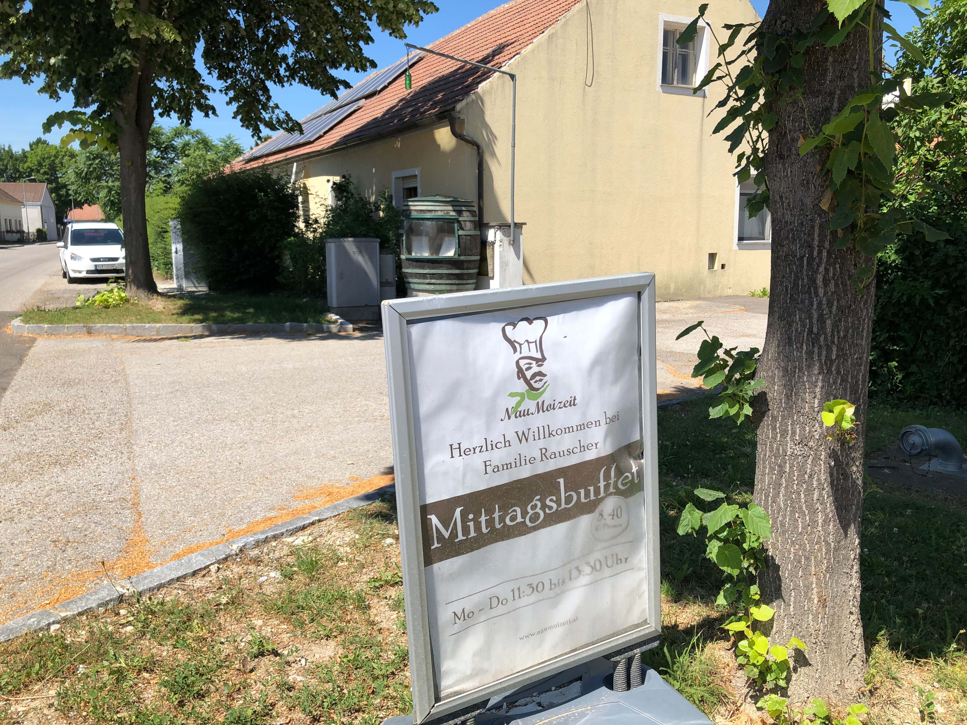 Nápis před budovou s nápisy "Mittagsbuffet" a "Herzlich Willkommen bei Familie Rauscher".