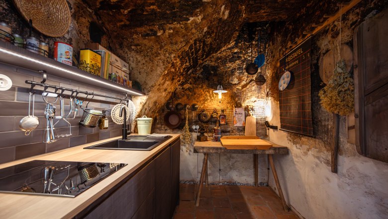 Rustik&aacute;ln&iacute; kuchyně se stěnami z př&iacute;rodn&iacute;ho kamene, dřevěn&yacute;m n&aacute;bytkem a modern&iacute;mi spotřebiči.