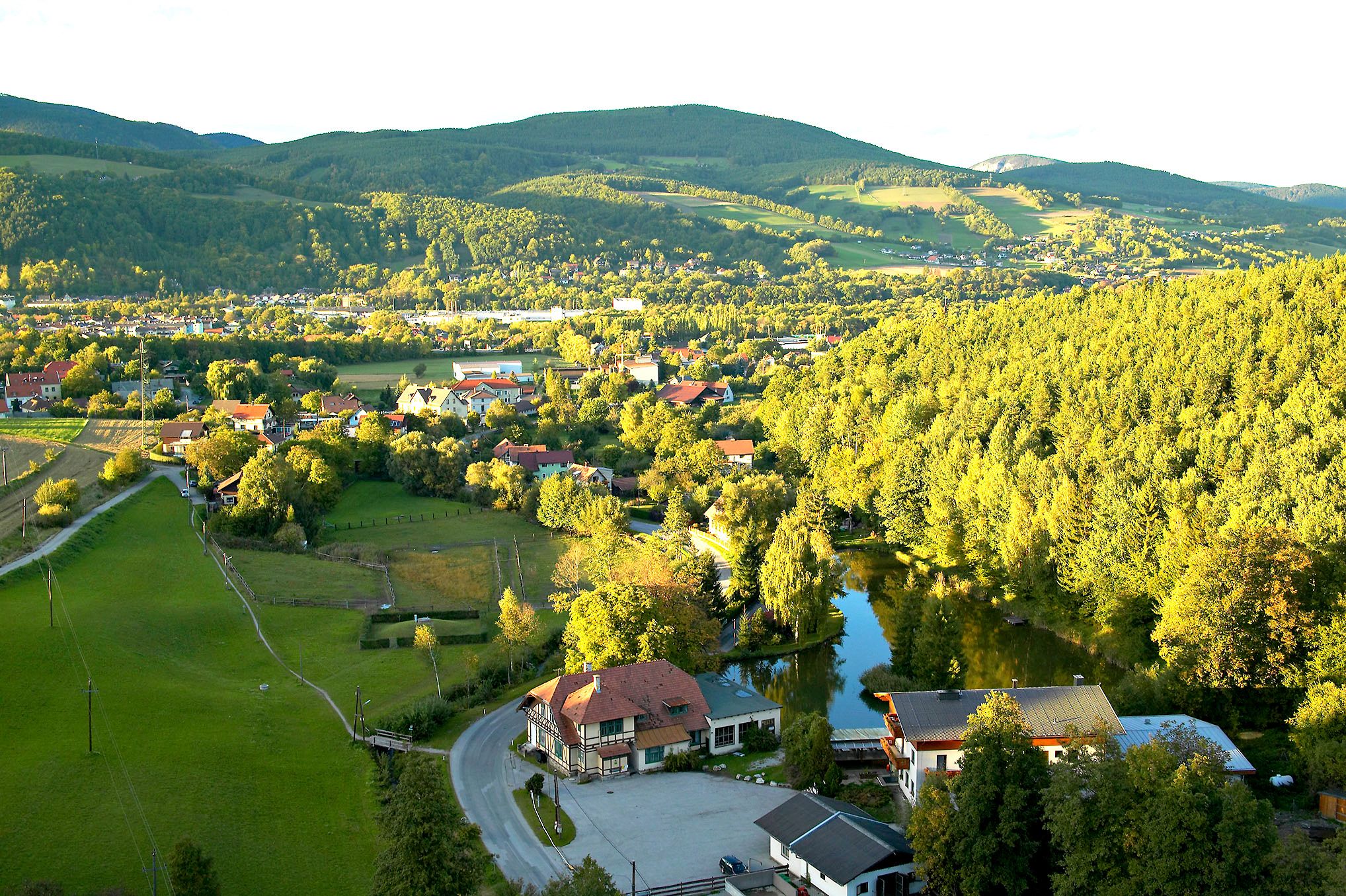 Pohled na krajinu Enzenreith s domy, lesy a kopci v pozadí.