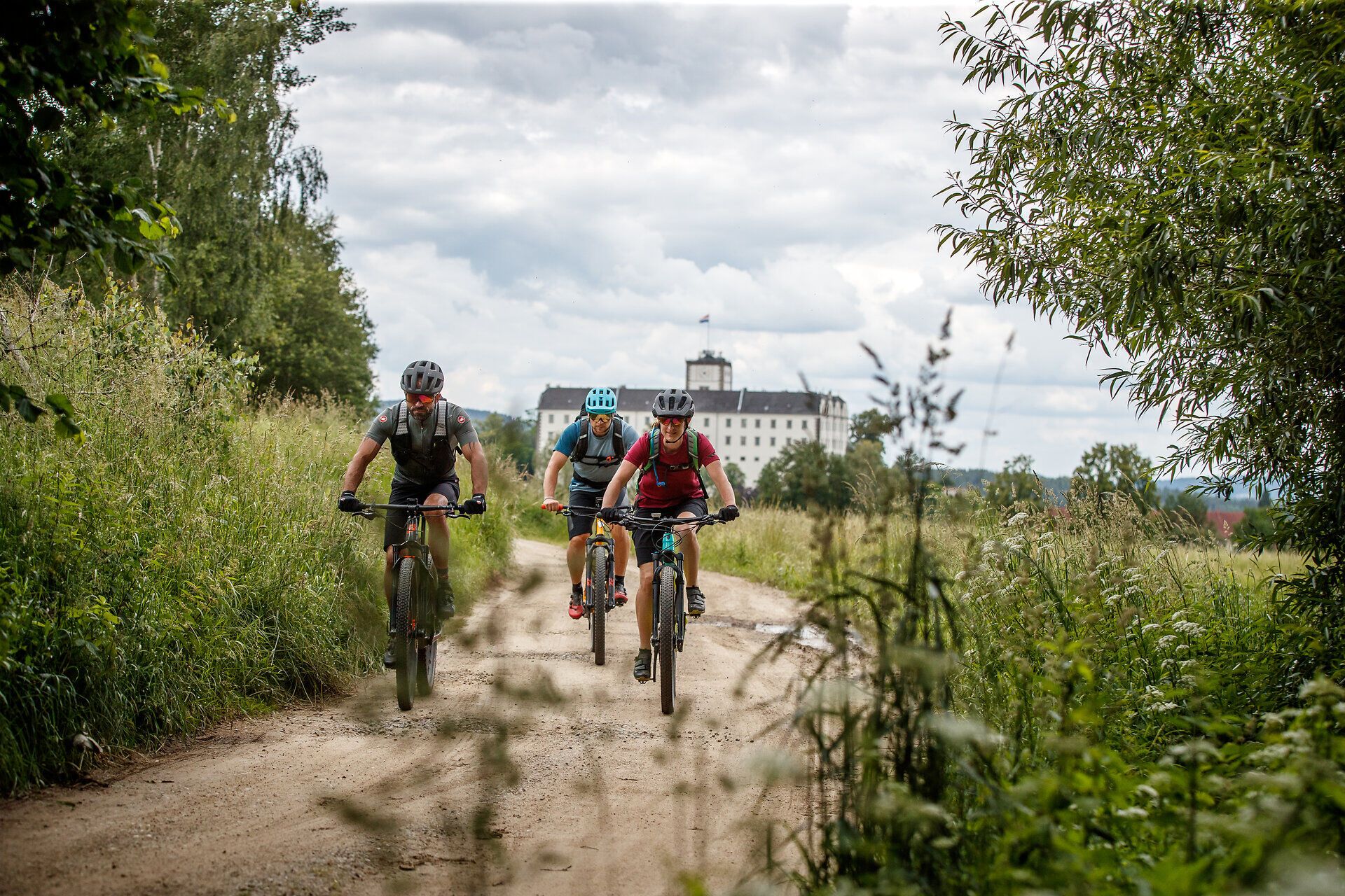 Tři horští cyklisté se řítí po úzké prašné cestě obklopené bujnou zelení a kopci. Svěží horský vzduch a dechberoucí scenérie vás zvou na nezapomenutelné dobrodružství. Zde, kde se příroda a sport setkávají, se každý okamžik stává zážitkem.
