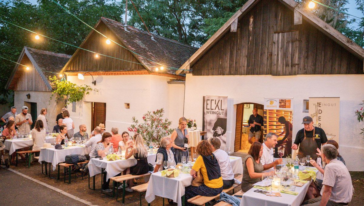 Lidé sedí u stolků před vinařstvím ve sklepních uličkách.
