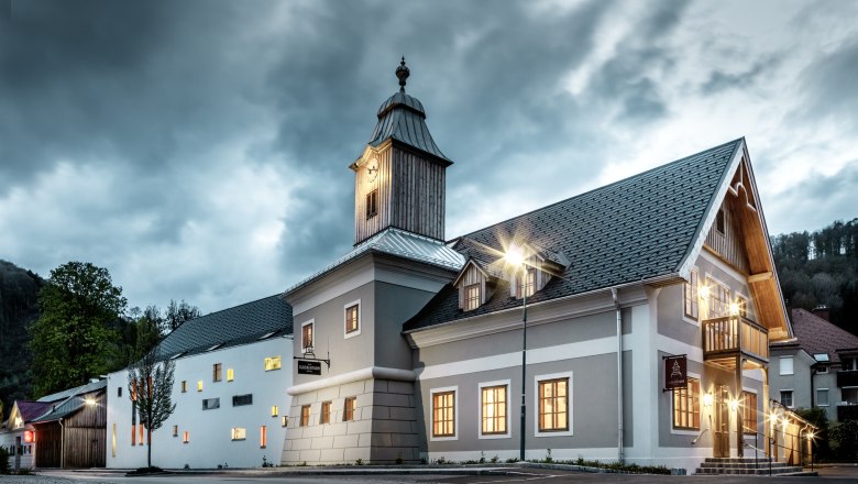 Hotel se zvonicí pod zataženou oblohou, osvětlený pouličními lampami.