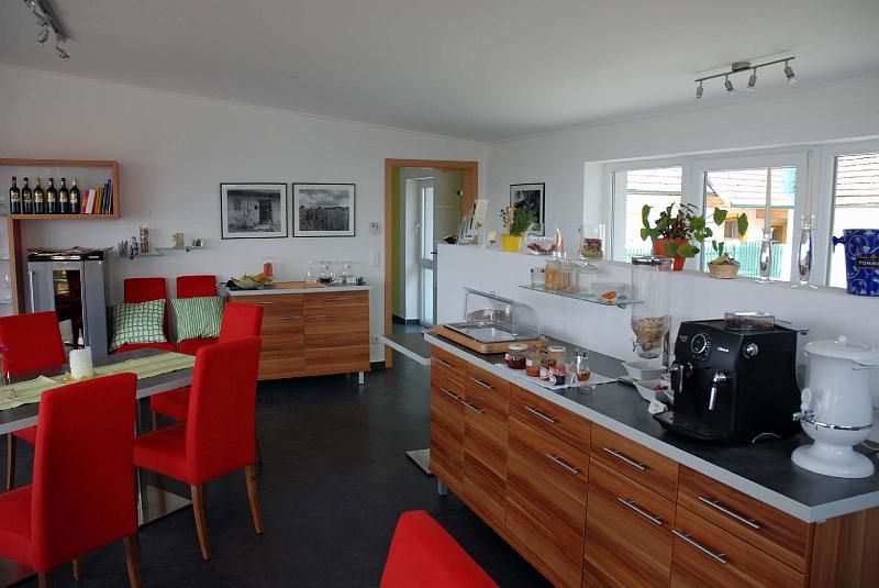 Snídaňová místnost s červenými židlemi, dřevěným nábytkem a kávovarem.