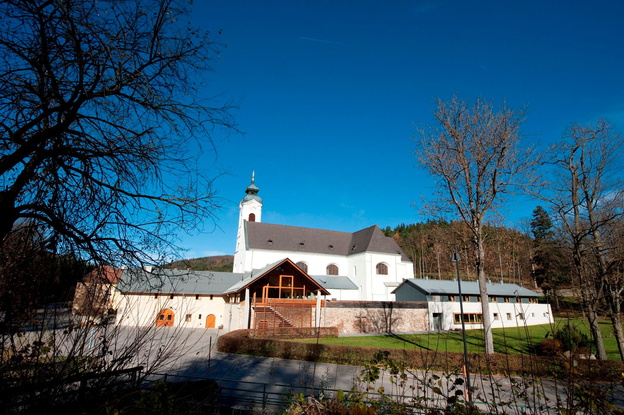 Poutní kostel Klein-Mariazell s modrou oblohou a stromy v popředí.