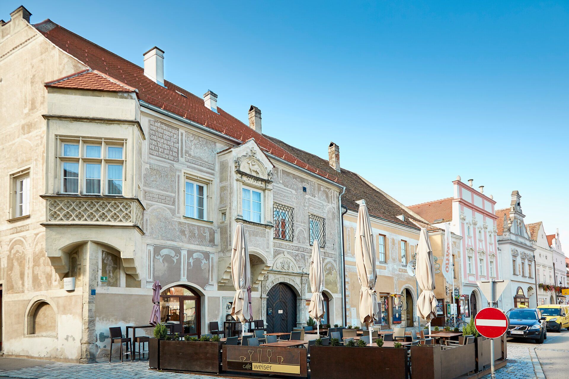 Historické budovy v Eggenburgu se zdobenými fasádami a pouliční kavárnou v popředí.