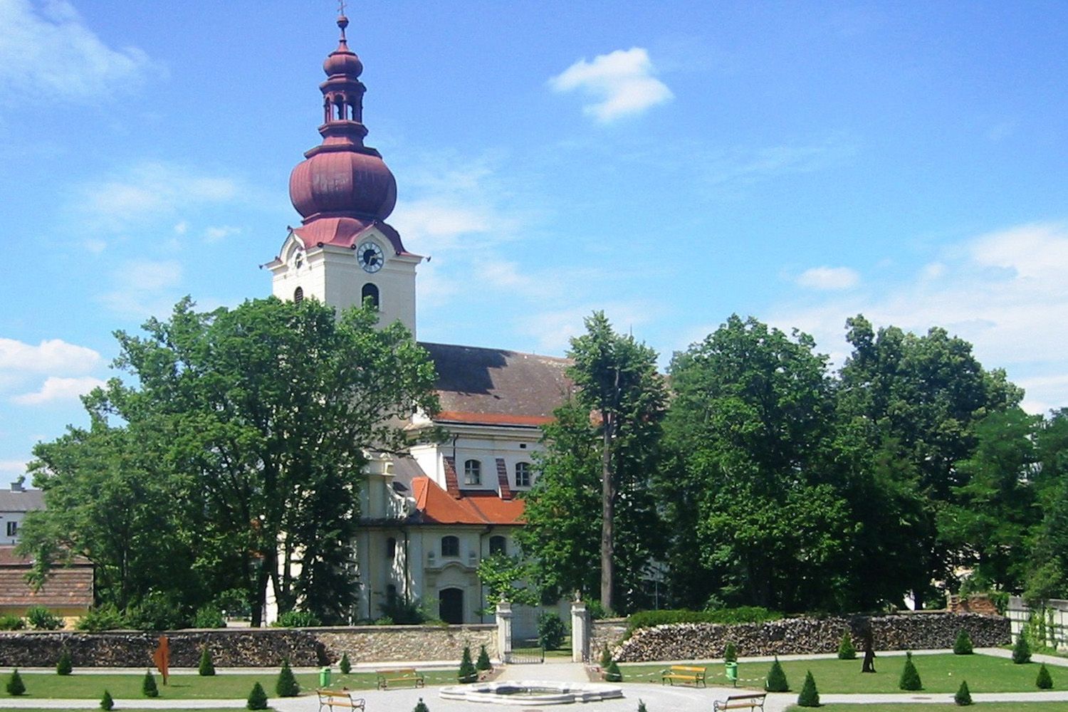 Barokní kostel s červenou věží a barokní zahradou v popředí.