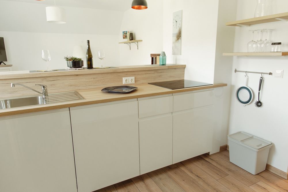 Moderní kuchyňská linka s dřevěnou pracovní deskou, dřezem, varnou deskou a policemi se sklenicemi.