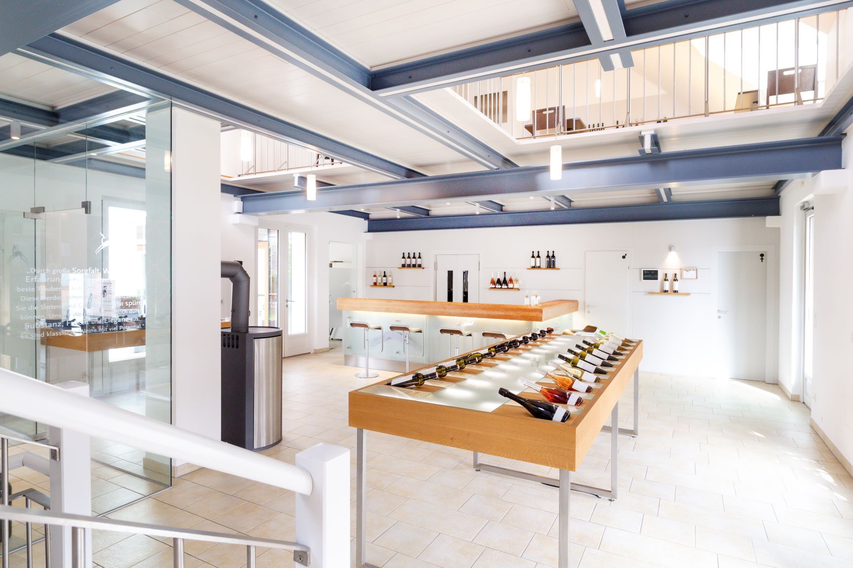 Pohled do interiéru moderní vinárny s lahvemi vína na stole a barem v pozadí.