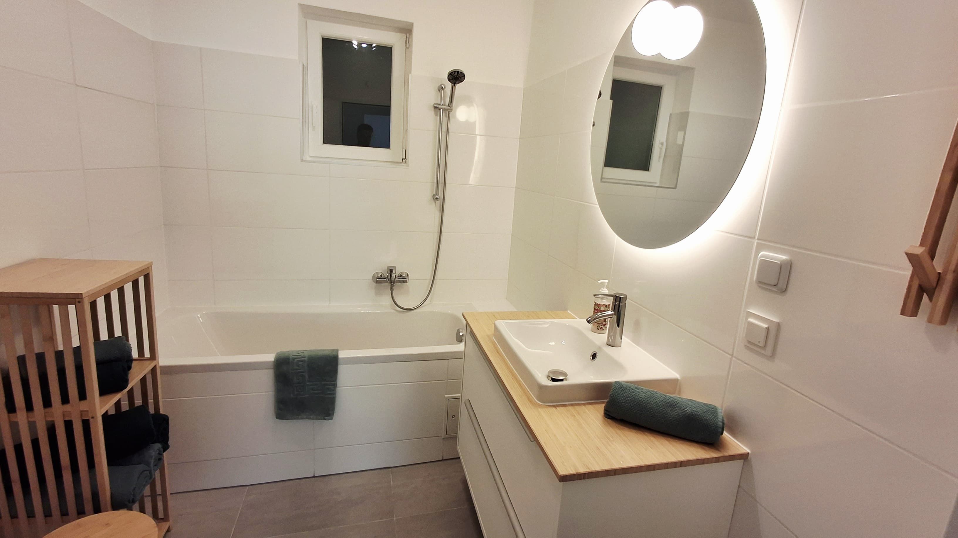 Moderní koupelna s vanou, umyvadlem a osvětleným zrcadlem.