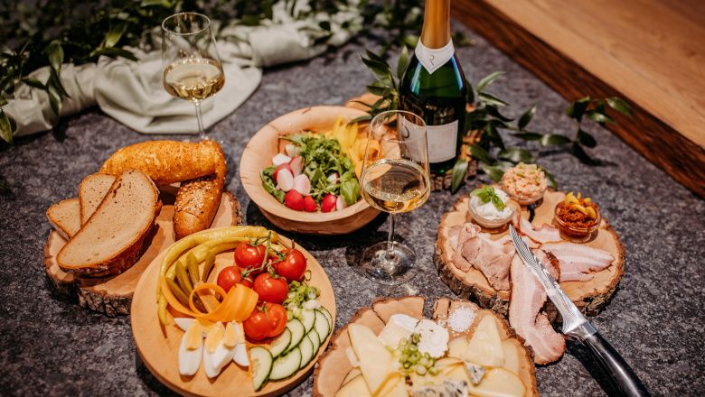 Různé pokrmy na dřevěných talířích s lahvemi vína a sklenicemi.