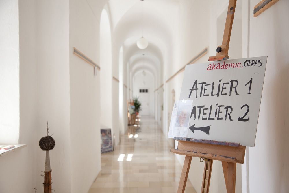 Světlá chodba s cedulí na stojanu, která ukazuje na ateliér 1 a ateliér 2.