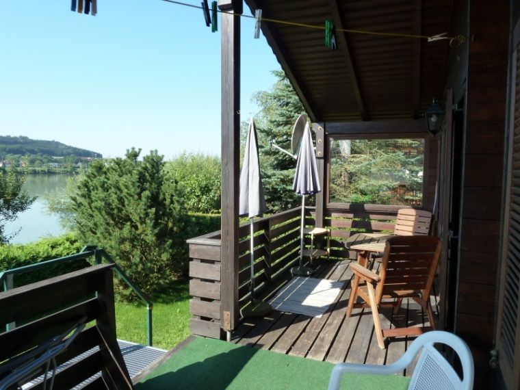 Dřevěná terasa rekreačního domu s výhledem na jezero a zelenou krajinu.