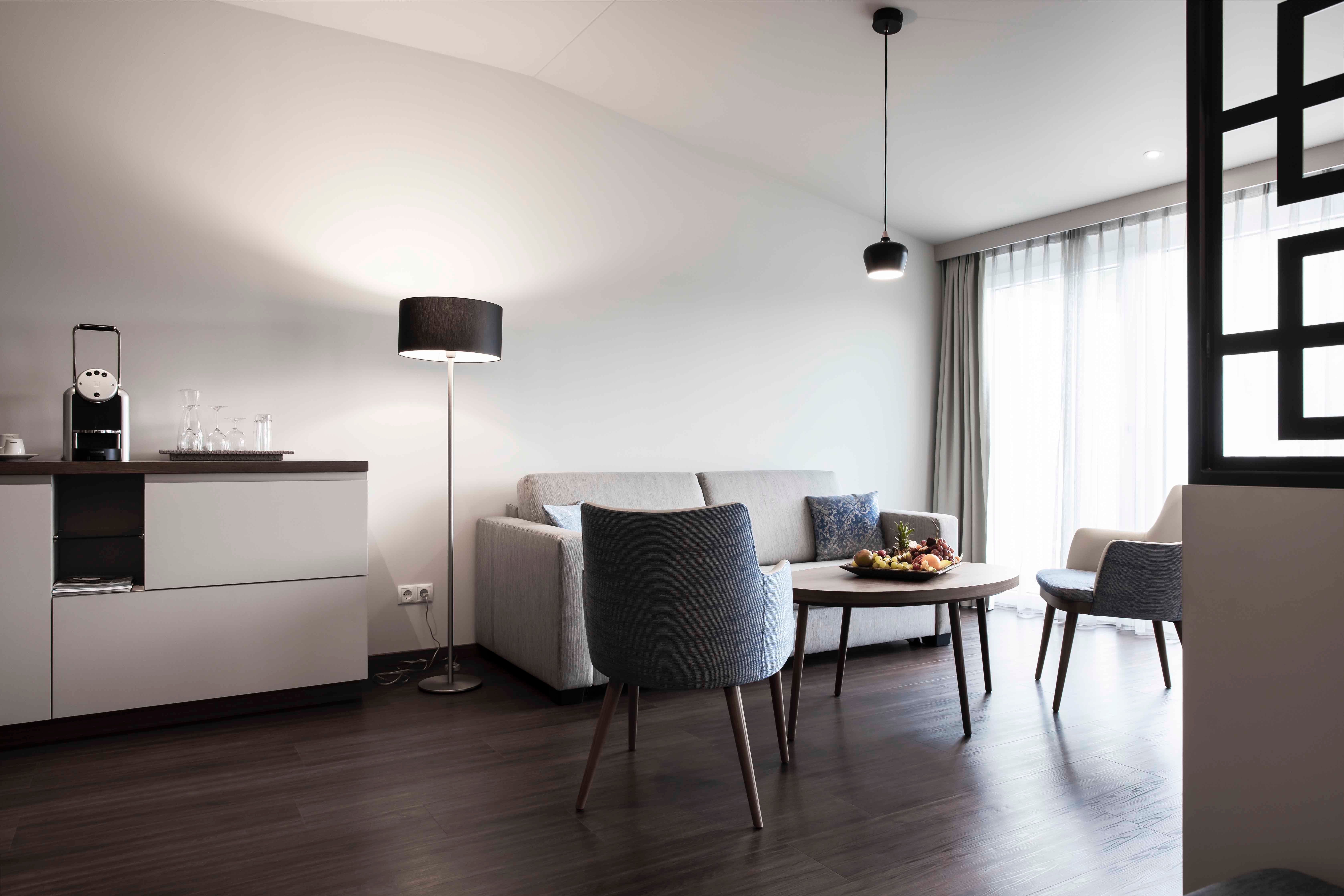 Moderní posezení s pohovkou, křeslem, stolem a stojací lampou ve světlé místnosti.