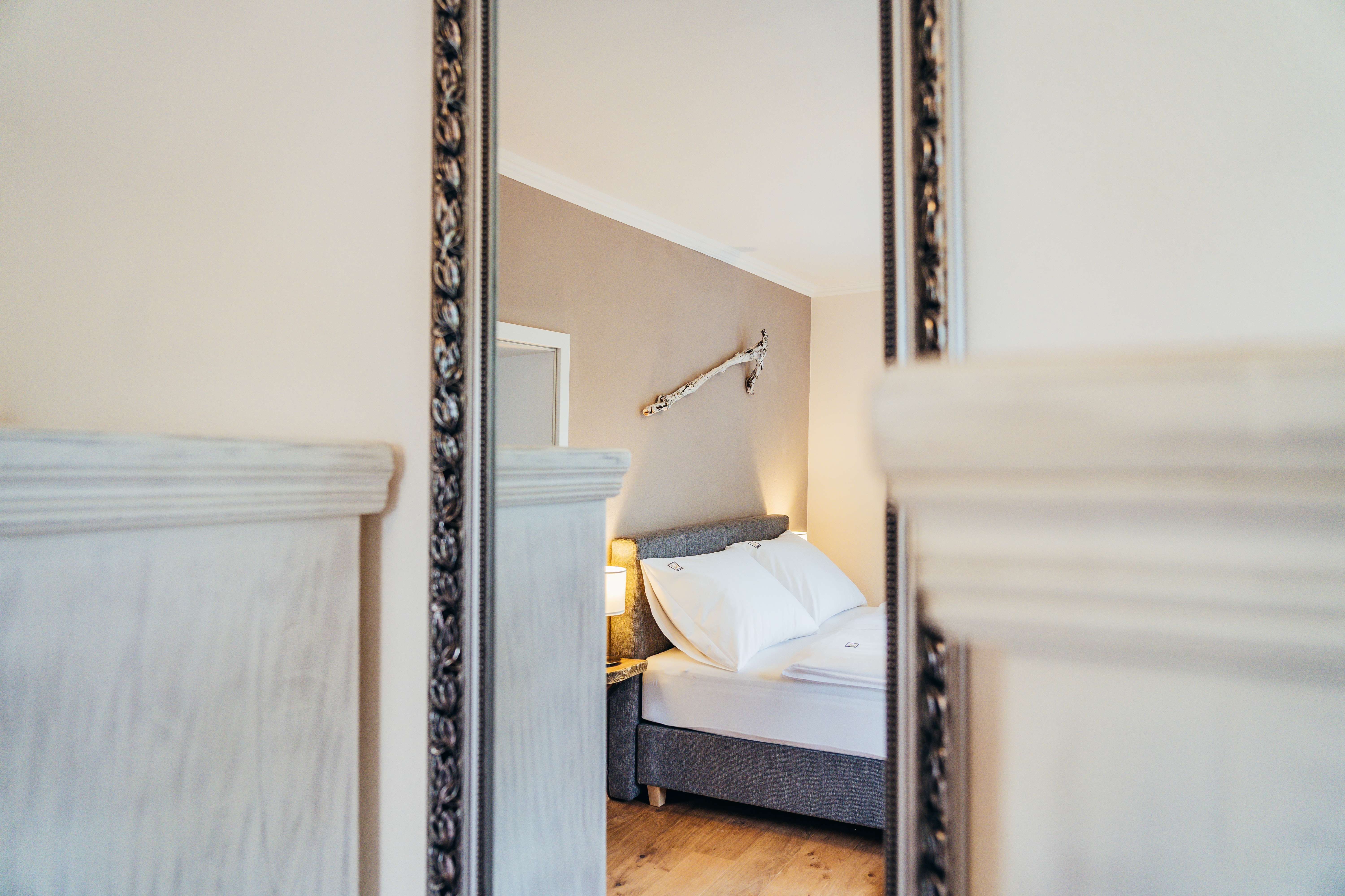 Zrcadlový obraz útulné ložnice s postelí a nástěnnou dekorací.