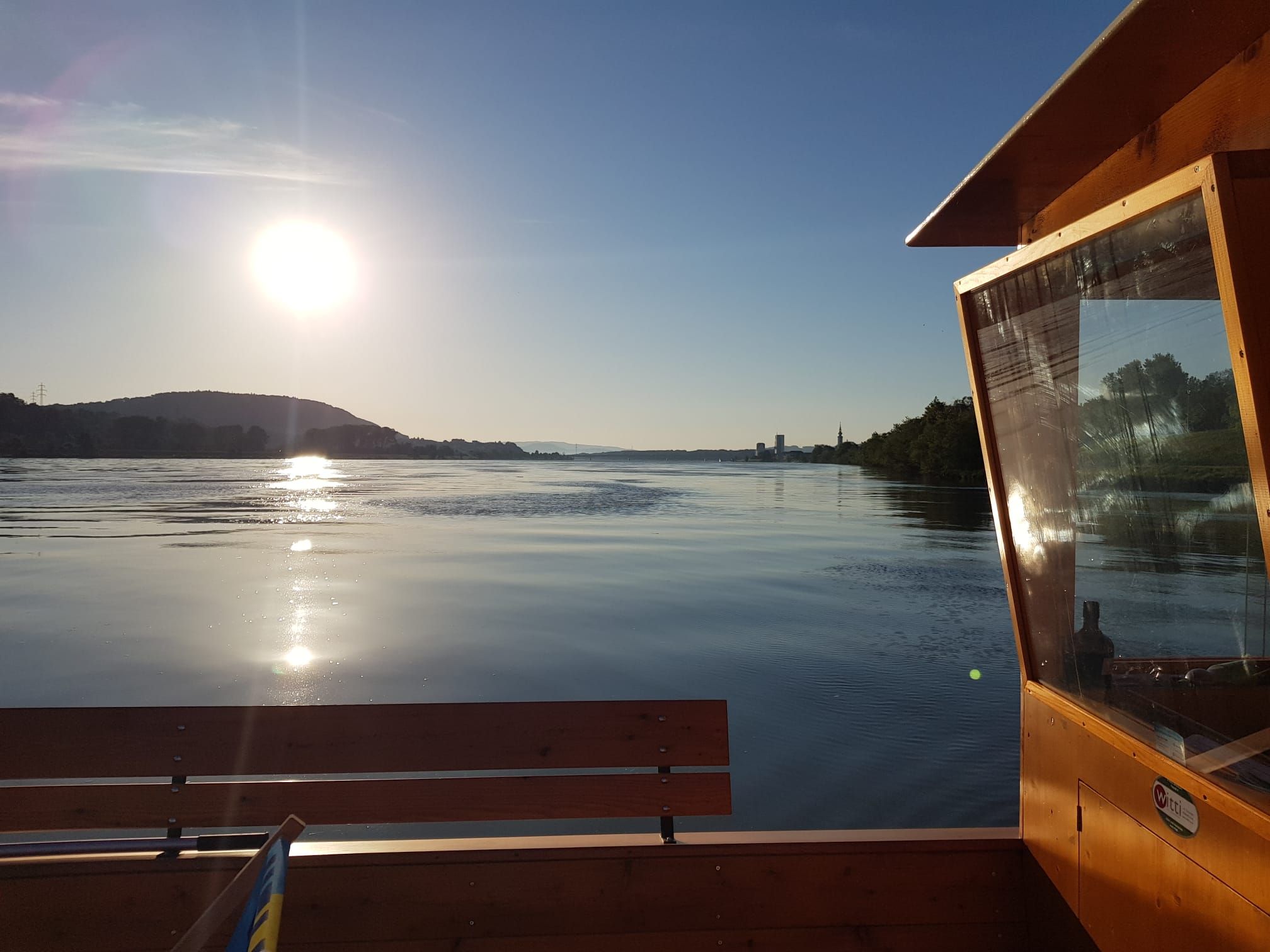 Západ slunce nad klidnou řekou s dřevěnou lodí v popředí.
