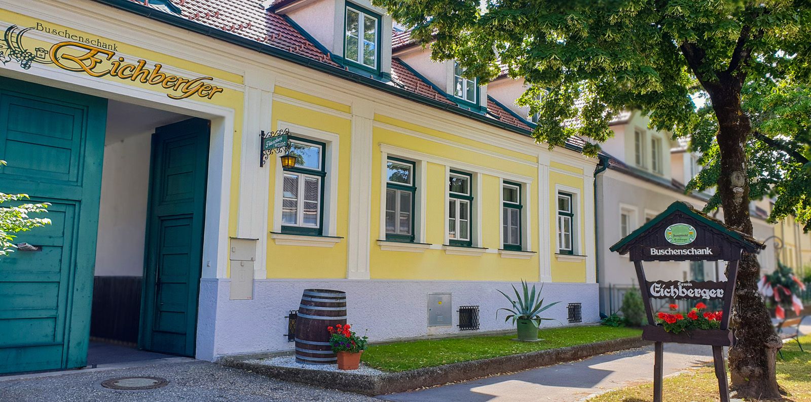 Žlutá budova se zelenými dveřmi a okny, nápis "Vinný šenk Eichberger", strom v popředí.