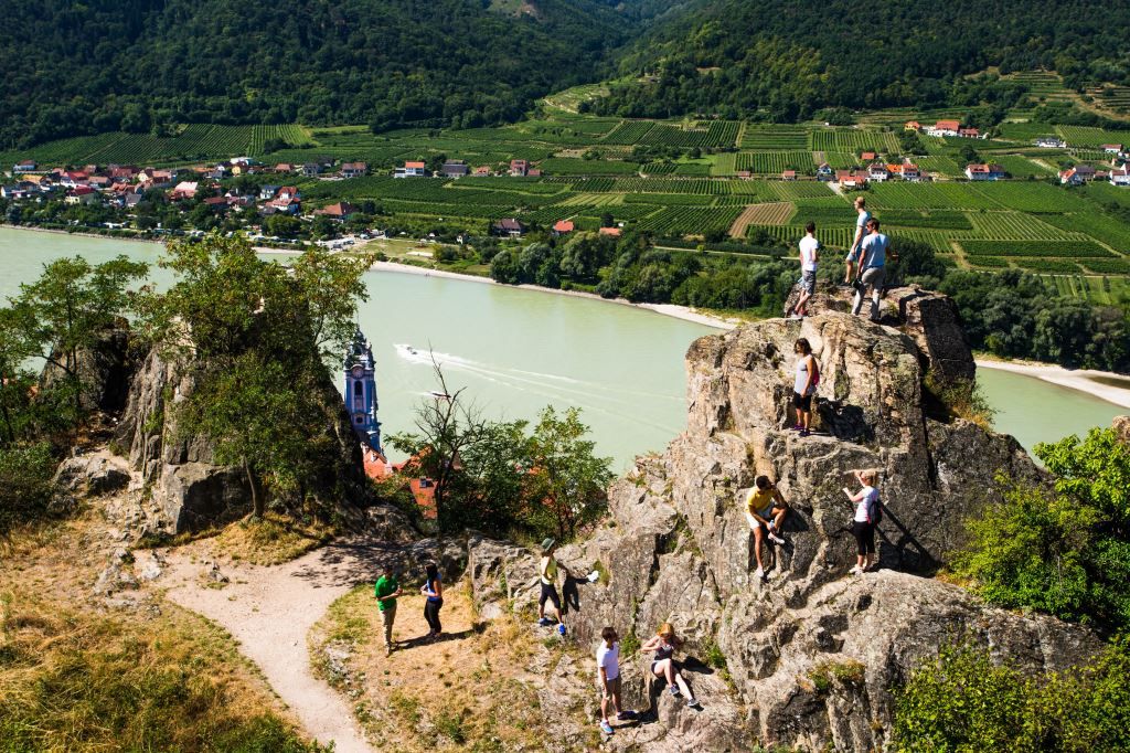 Lidé lezou po skalách s výhledem na Dunaj a vinice v Dürnsteinu.