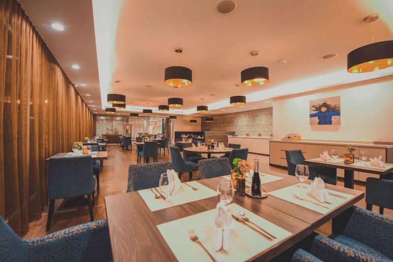 Elegantní restaurace s prostřenými stoly, modrými židlemi a moderním osvětlením.