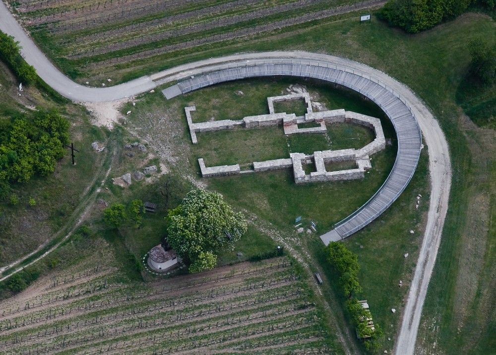 Letecký pohled na místo archeologických vykopávek s půlkruhovou lávkou.