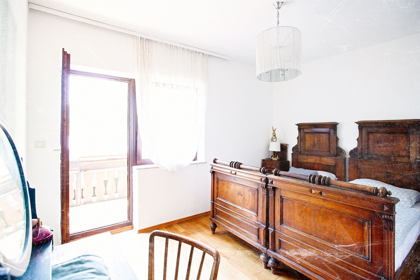 Světlá ložnice se starožitným dřevěným nábytkem a vstupem na balkon.