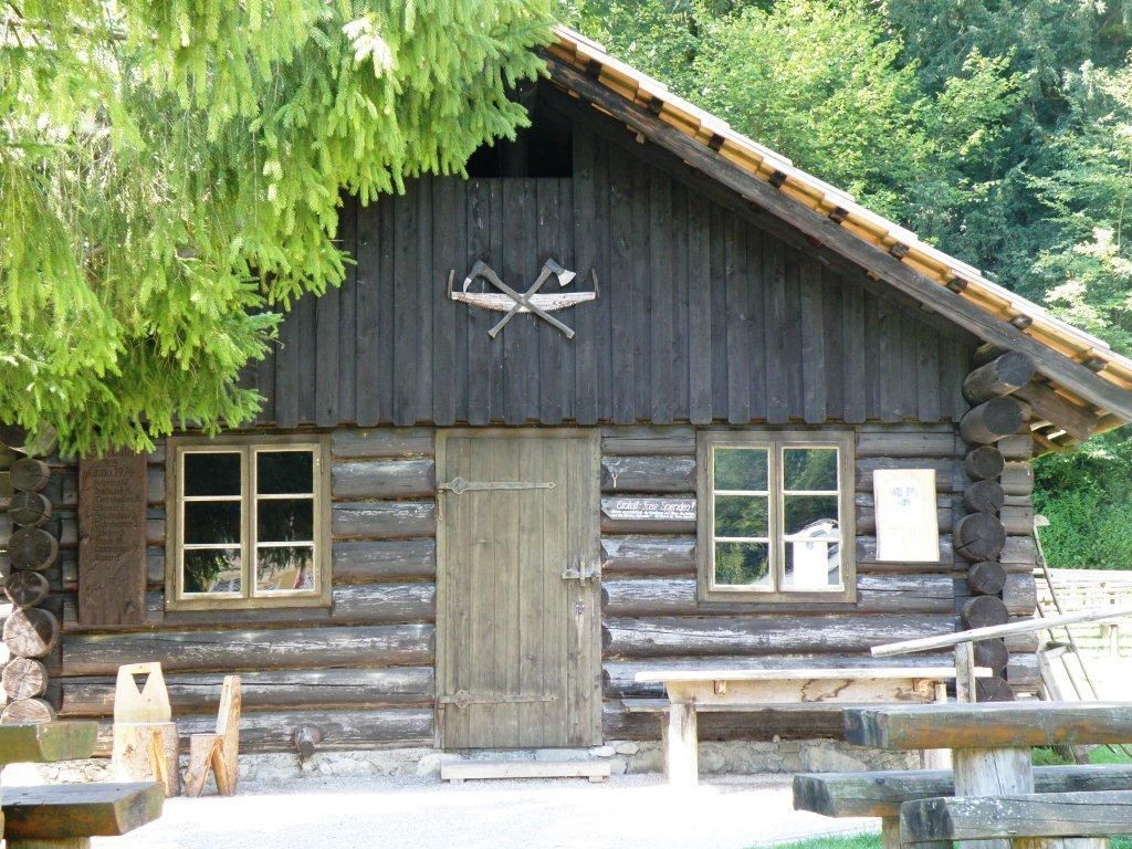 Dřevěná chata se dvěma okny a dveřmi, obklopená stromy.