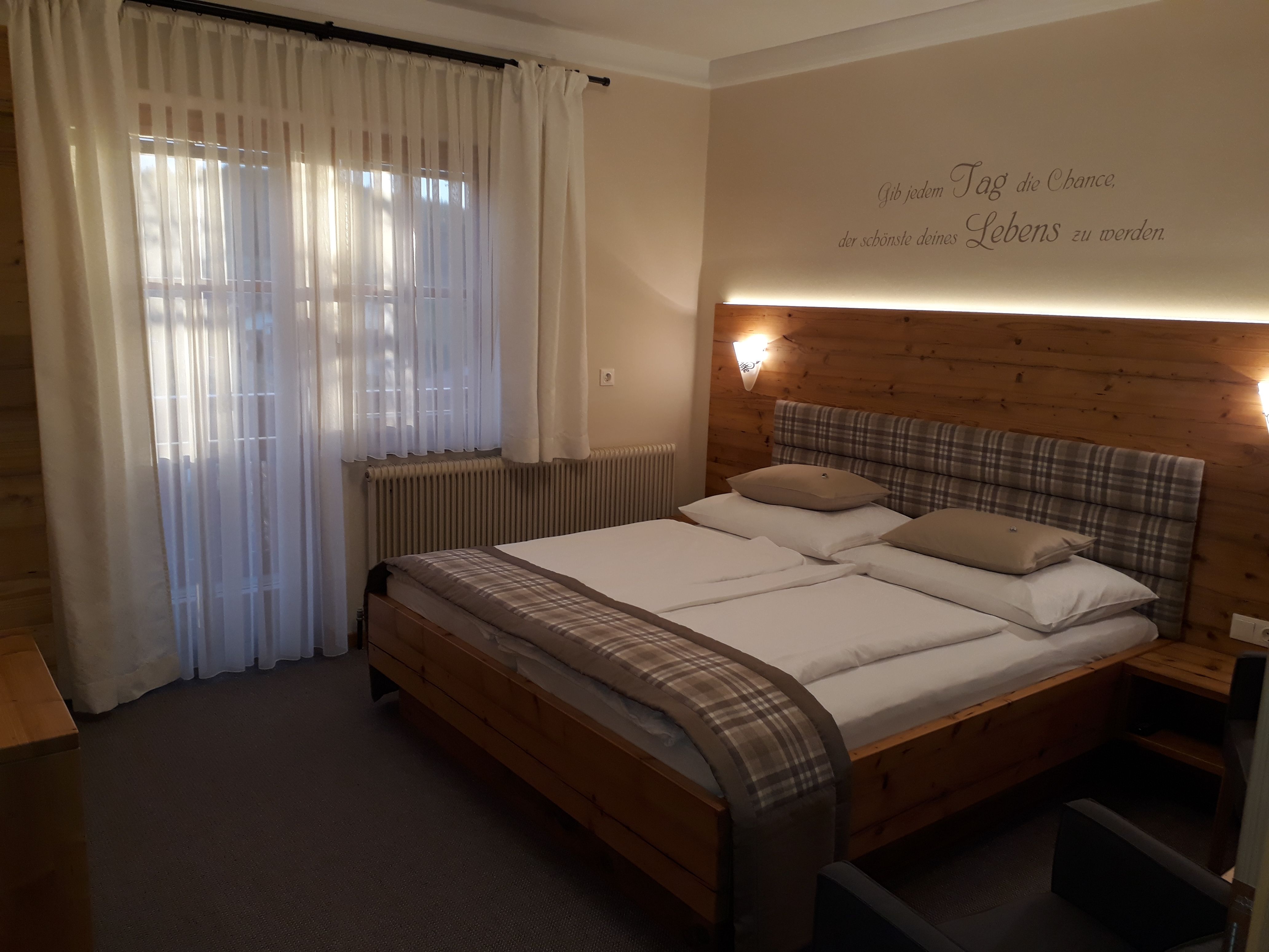 Útulná ložnice s manželskou postelí, dřevěnou stěnou a závěsy.