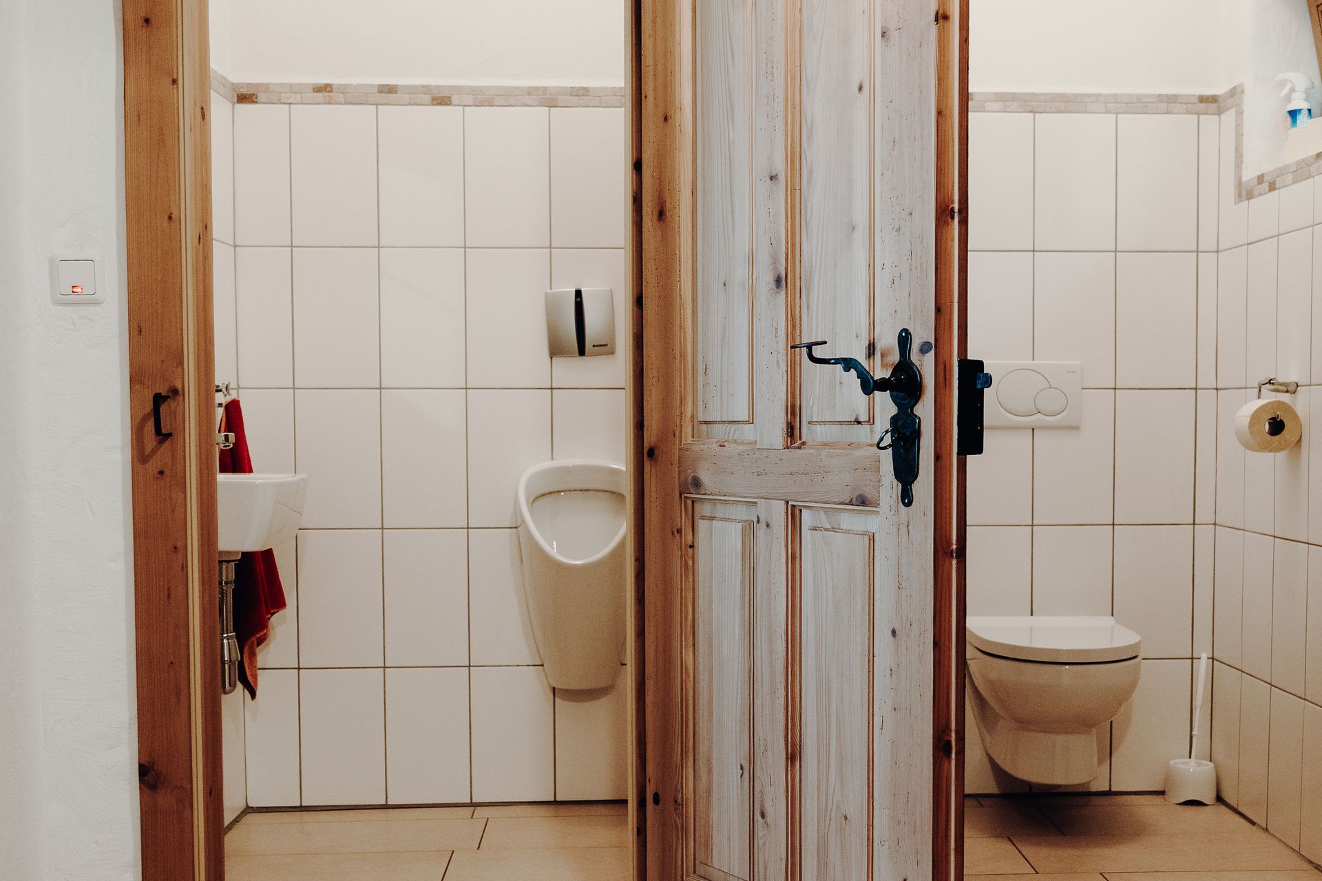 Dvě toalety s dřevěnými dveřmi, vlevo pisoár a umyvadlo, vpravo toaleta.