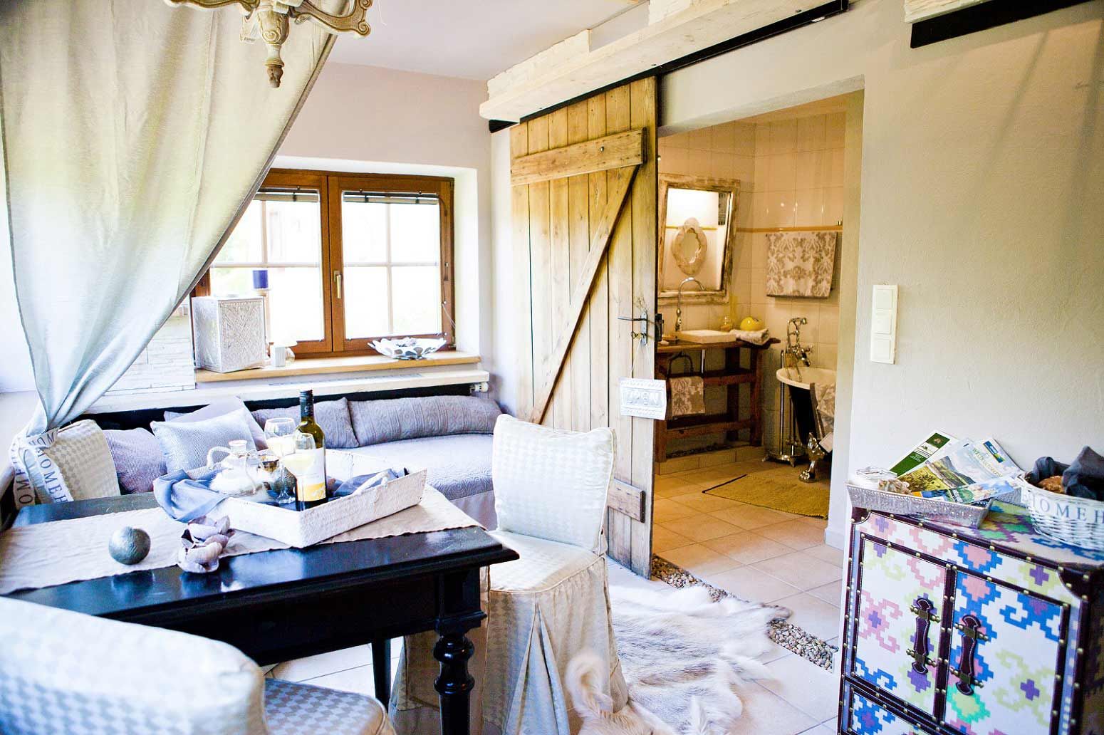 Útulný obývací pokoj s dřevěnými dveřmi, pohovkou, stolem a dekorativními prvky, výhled do koupelny.