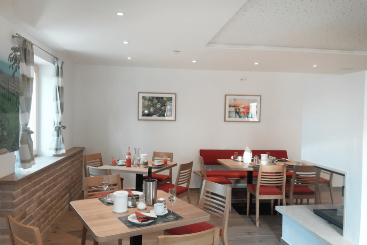 Útulná snídaňová místnost s dřevěnými stoly, červenými čalouněnými lavicemi a dekorativními obrázky na stěnách.