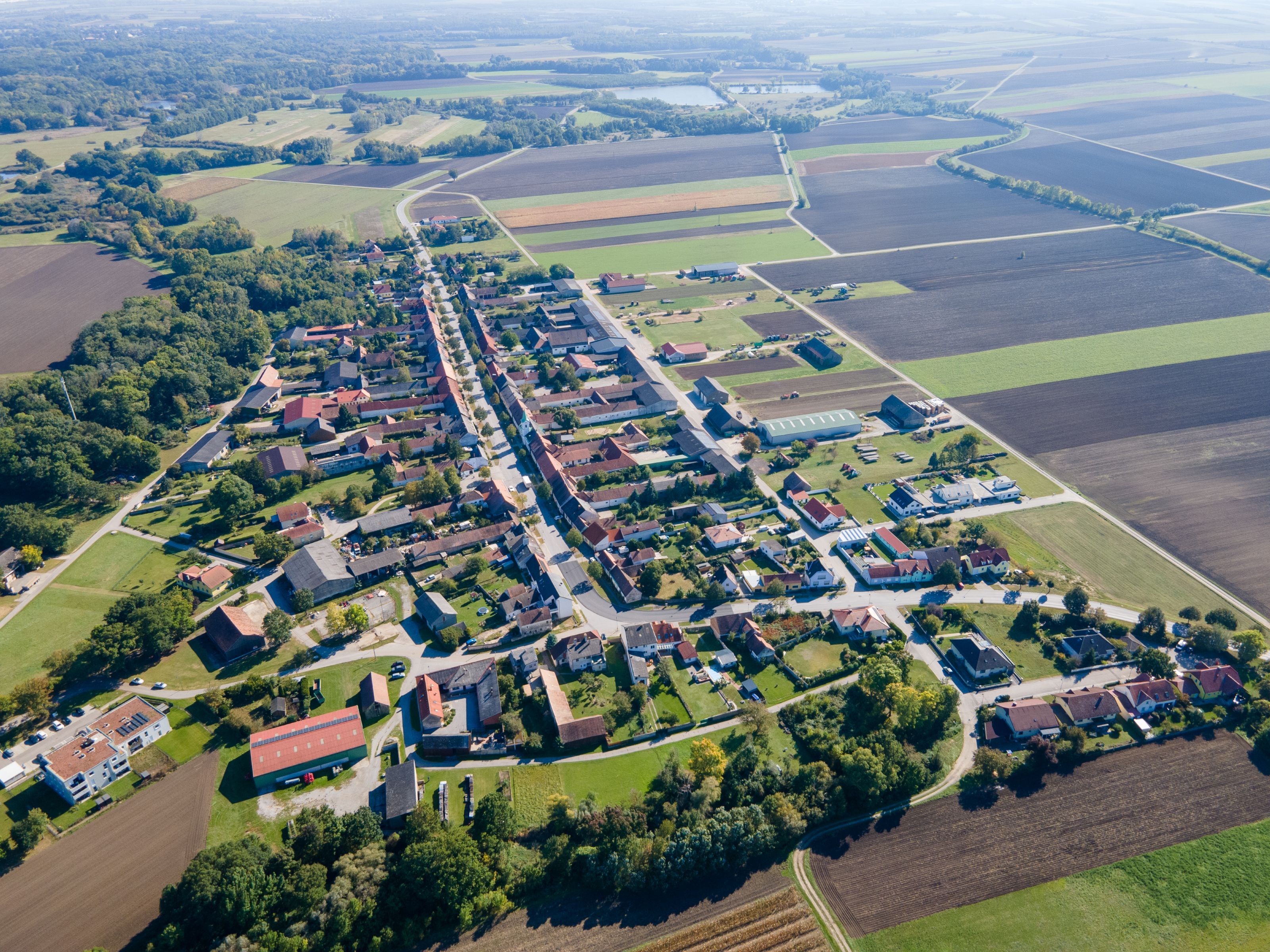 Letecký snímek obce Weiden an der March s centrem obce, poli a lesními pásy v okolí.