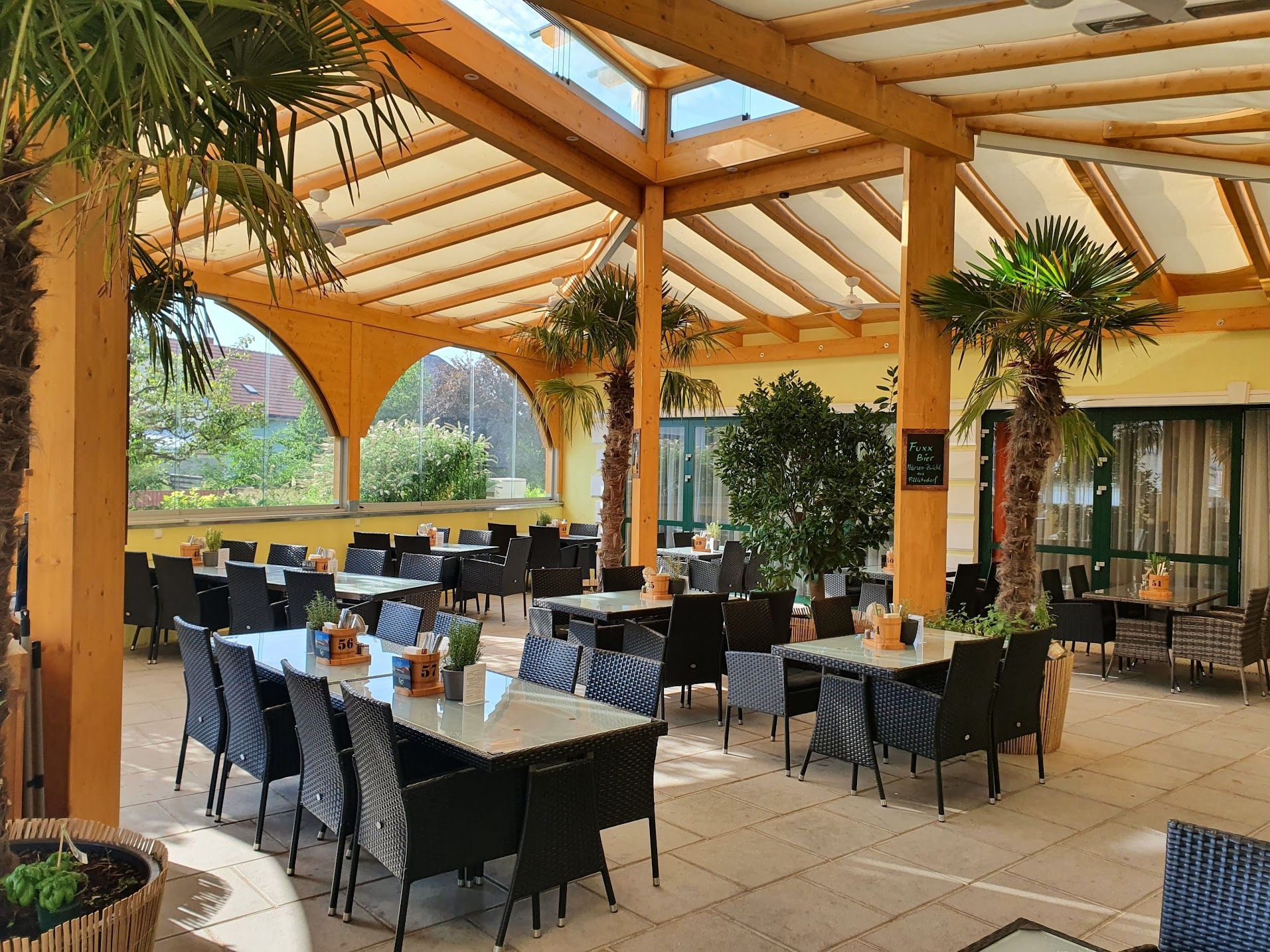 Krytá terasa restaurace s palmami a stoly.